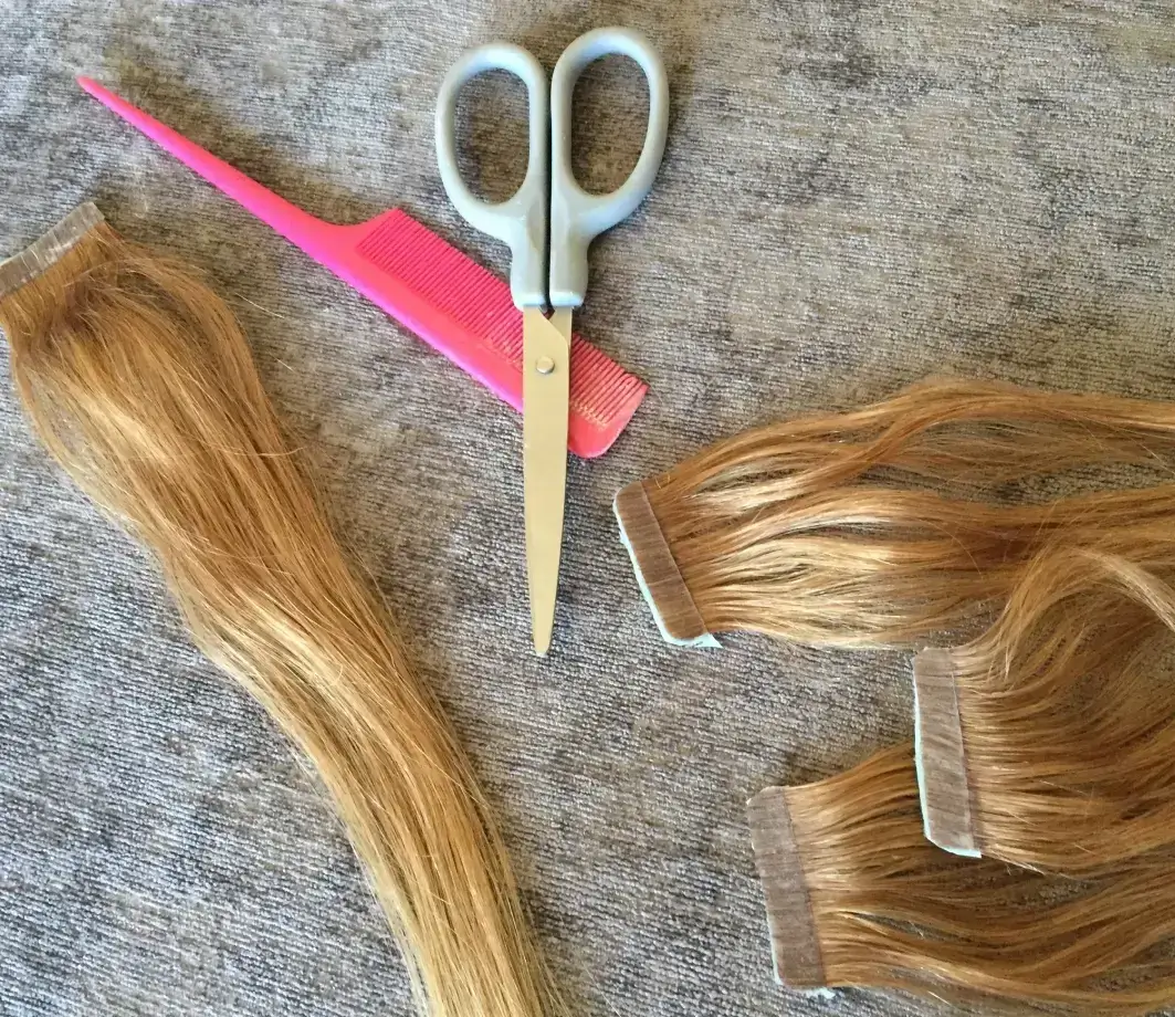 Hair extensions, scissors, and a comb on a gray surface.