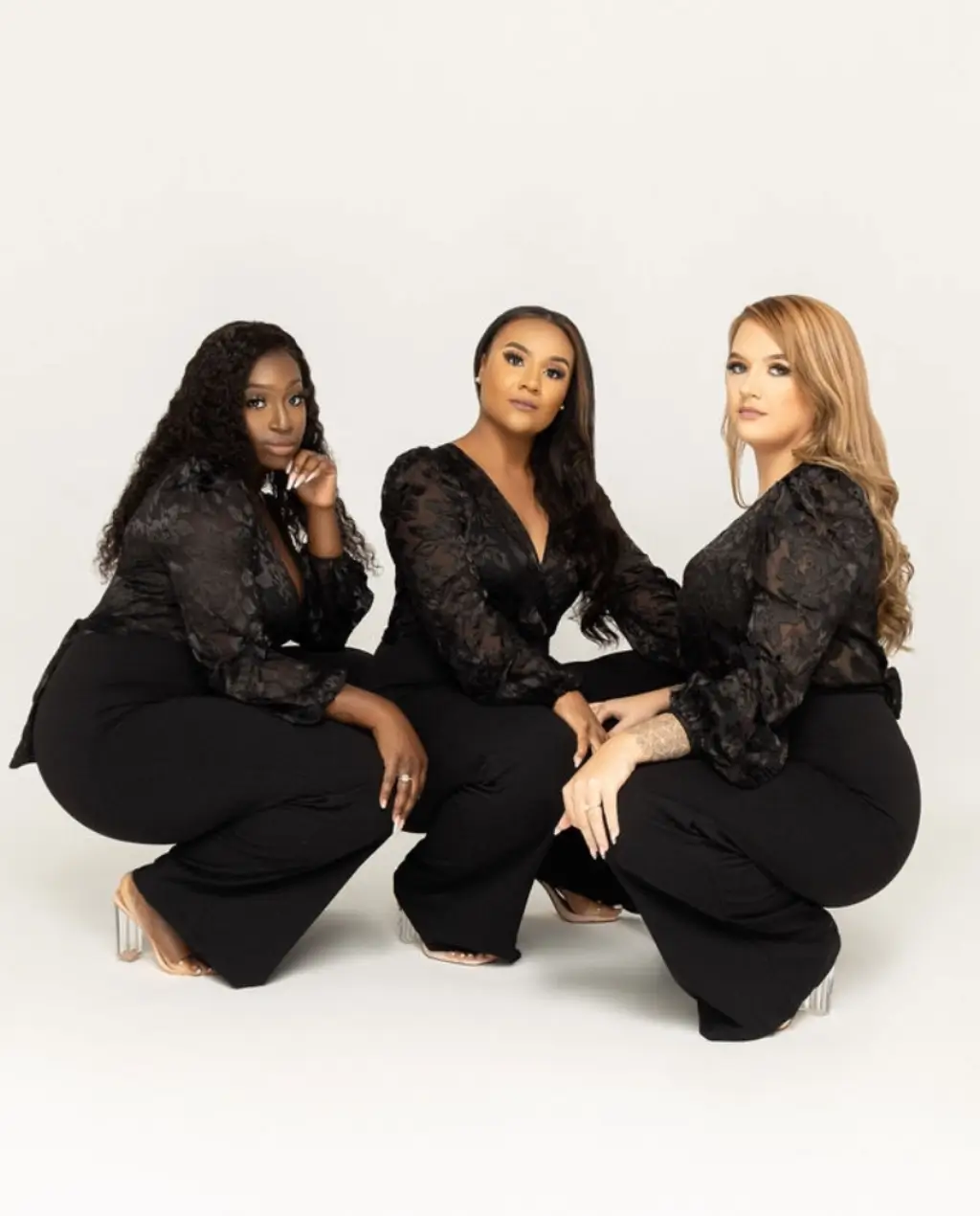Three women in black outfits posing confidently.